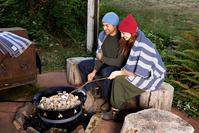 Couple wrapped up in a Denim Blue Northwest Wool Throw roasting marshmallows in their backyard fire pit.