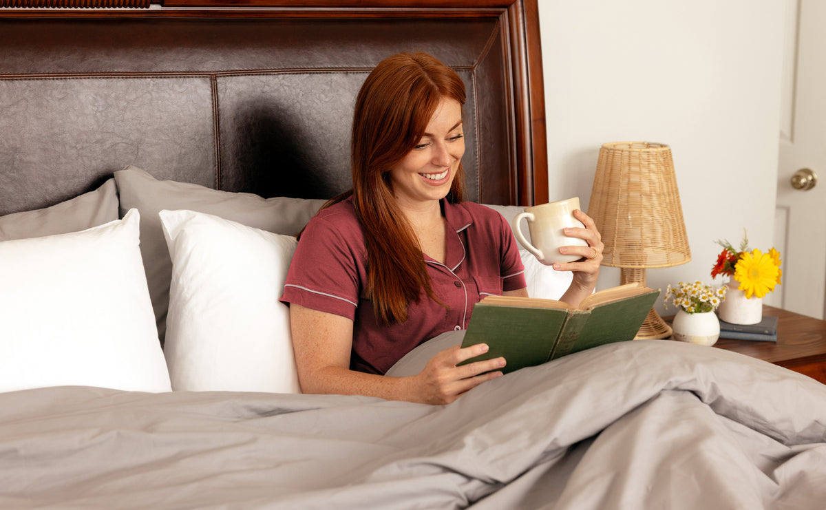 Woman relaxing in bed reading. The bed is made with Carolina Gray Heritage American Sheets.