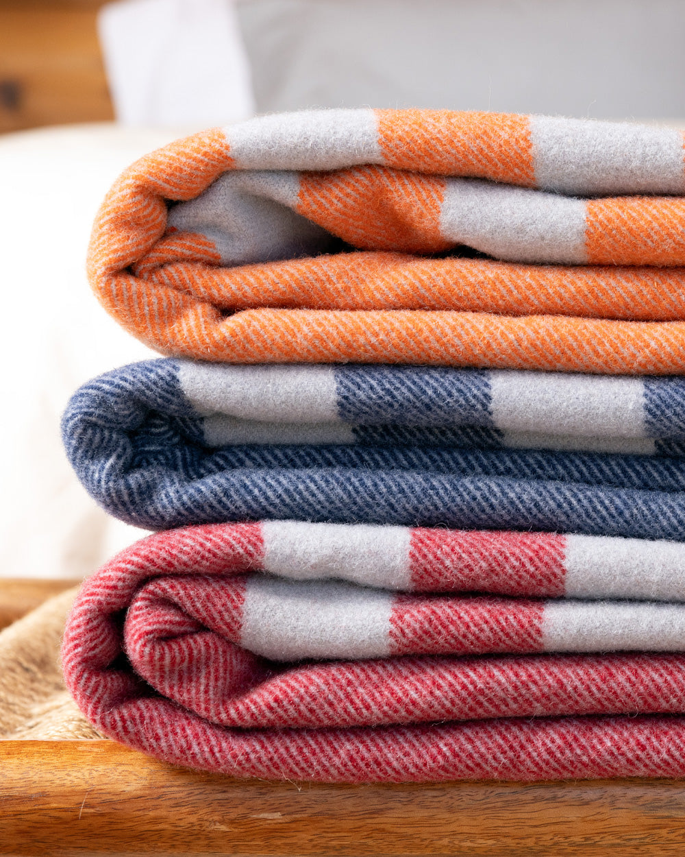 Three Northwest Wool Throws (in Mesa Sunset, Denim Blue, and Rainier Red) folded and stacked on a bench.