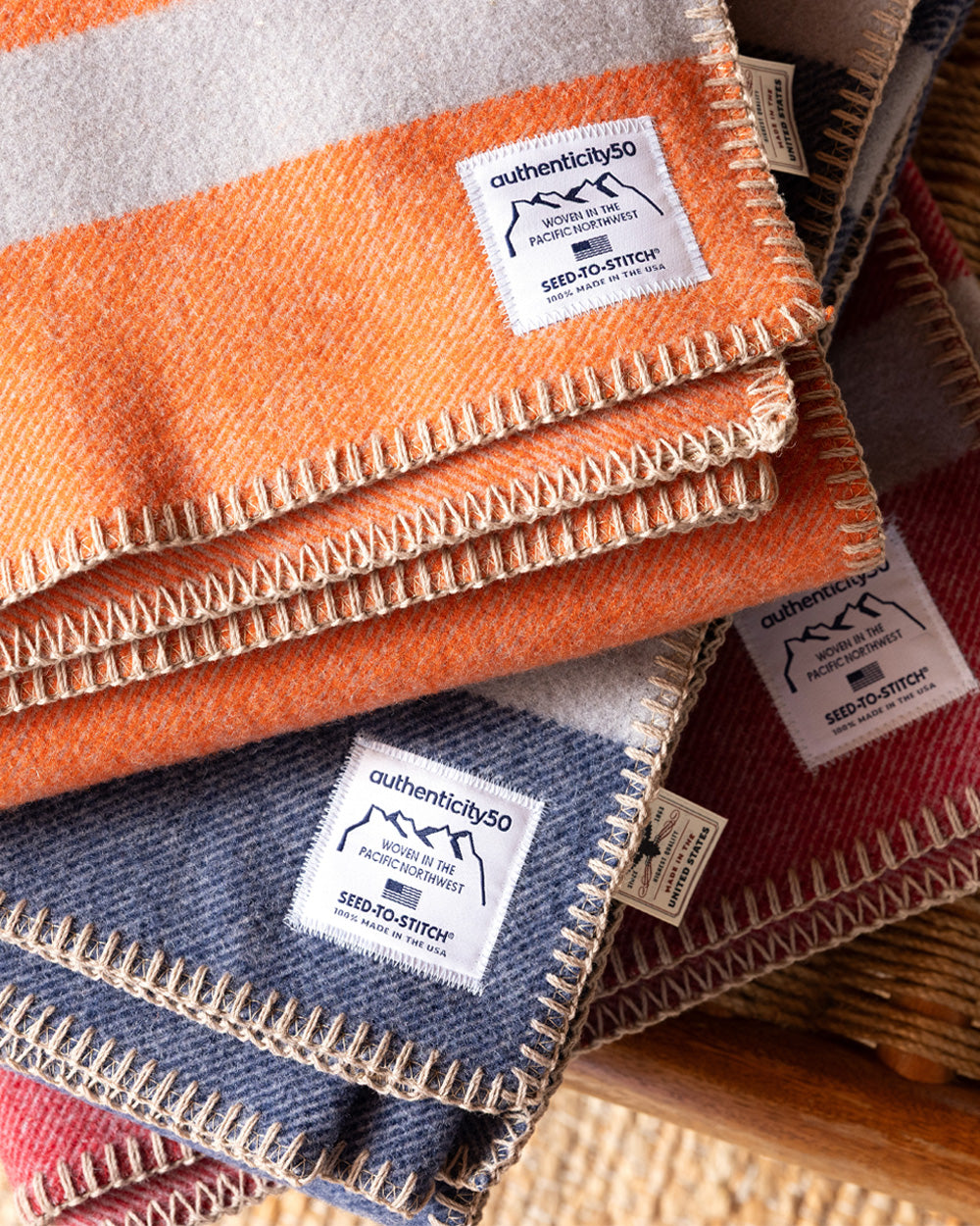 Three Northwest Wool Throws (in Mesa Sunset, Denim Blue, and Rainier Red) folded and stacked on a bench.