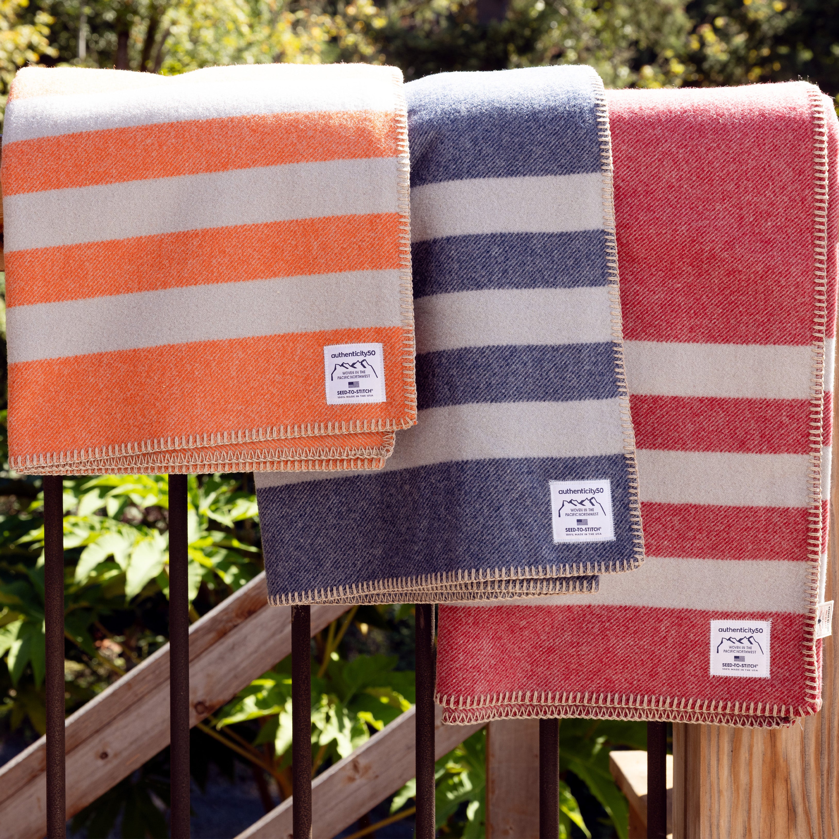 Folded Northwest Wool Throws (in Mesa Sunset, Denim Blue, and Rainier Red) draped over the railing of a deck.